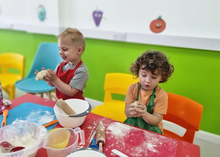 Two young children engaged in cooking activities at a table with ingredients and bowls.