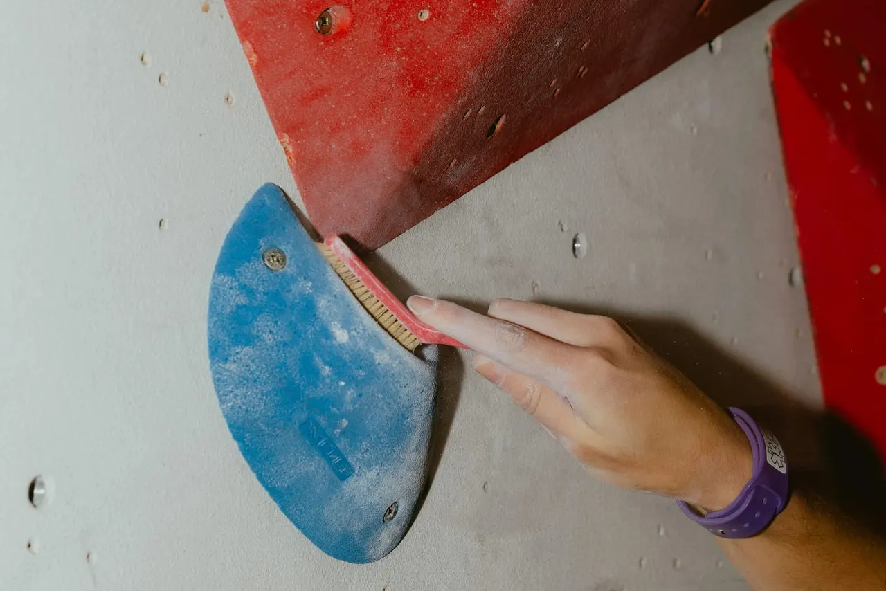 Person's hand gripping a blue climbing hold on an indoor rock climbing wall with red and white panels.