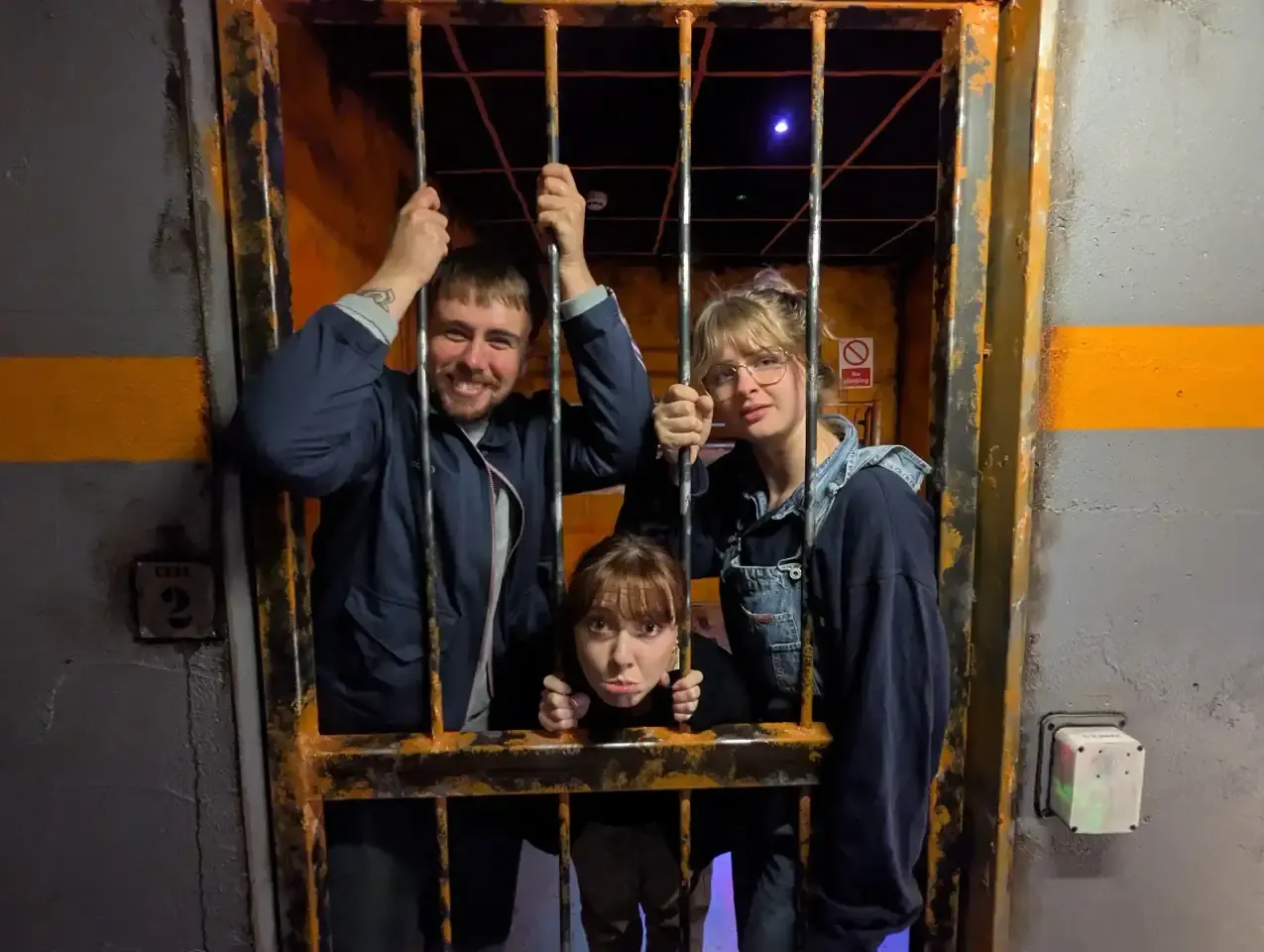 Four visitors posing playfully behind a large barred prison cell prop during an escape room experience.