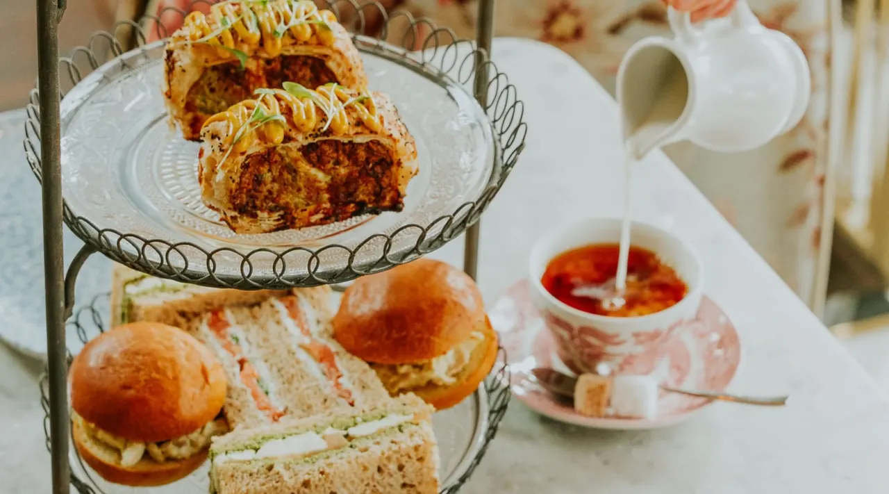 Tiered stand displaying afternoon tea with sliced cake, sandwiches, jam and cream service.
