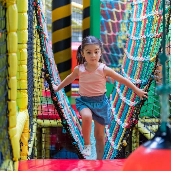 Young child navigating through a colourful net tunnel in an indoor play area.