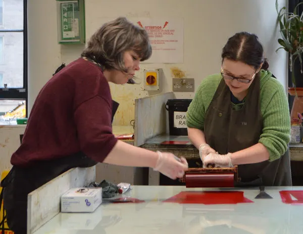 Two people working together at a printing press in a workshop studio.