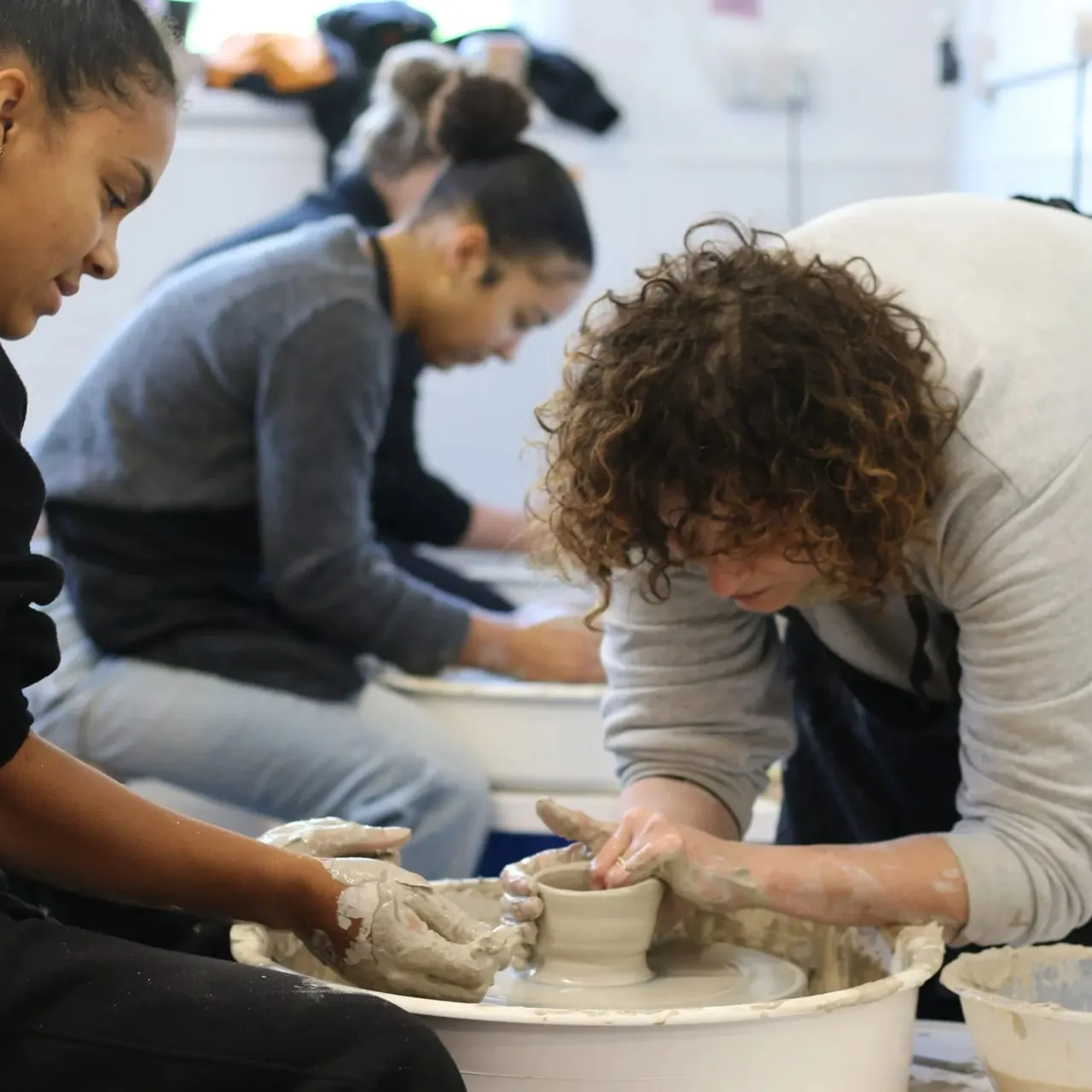 Children and an adult working together at a pottery wheel, shaping clay during a hands-on ceramics class.