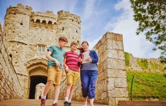 Three children running past stone castle towers on a sunny day.