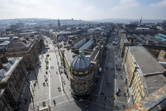 Elevated view of a city centre with historic buildings, a domed structure, pedestrian streets and distant hills.