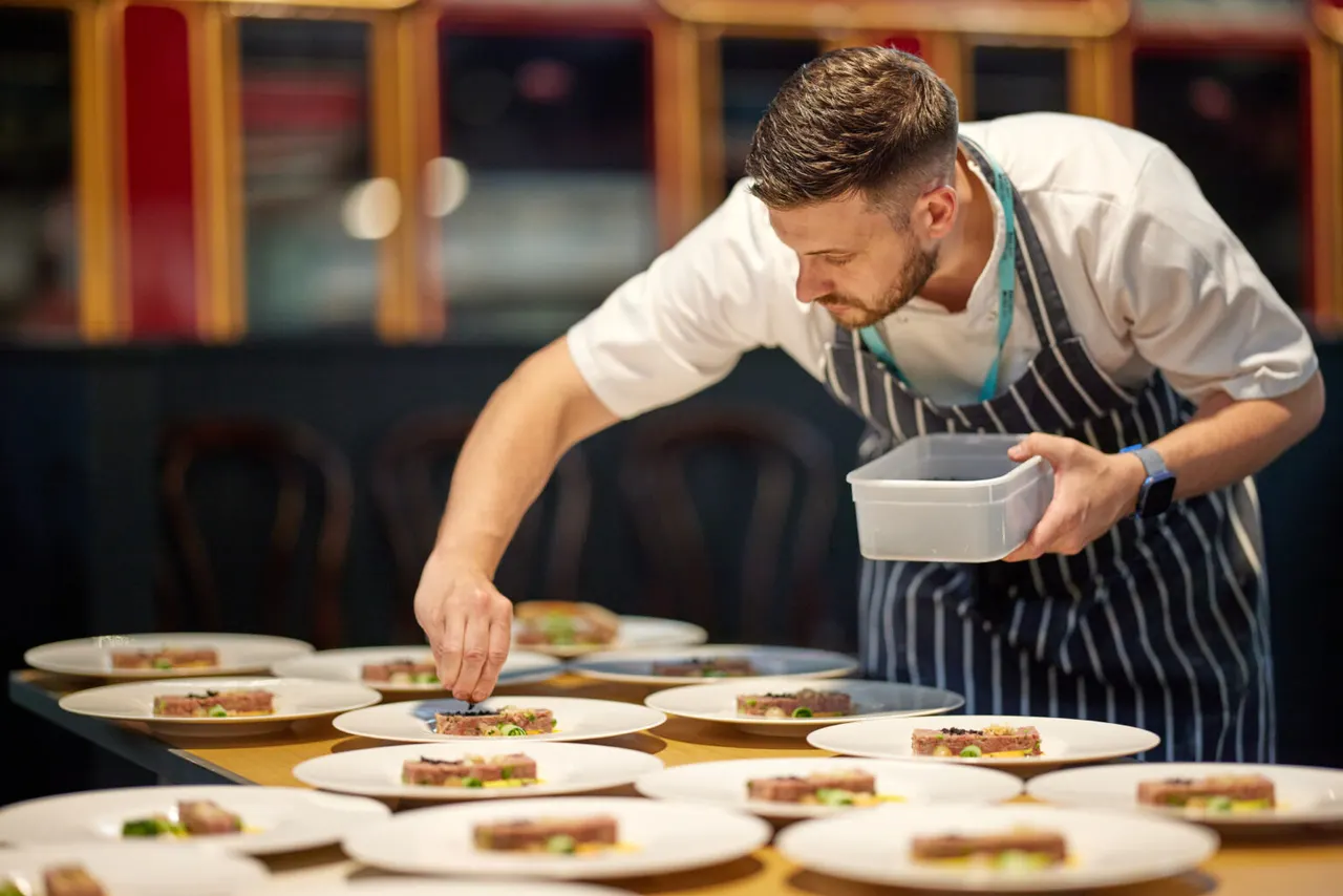 Chef plating up dishes at a fine dining event in an elegant restaurant setting.