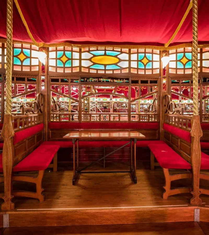 Ornate vintage-style fairground booth with red velvet interior, decorative wooden frame and stained-glass panels.