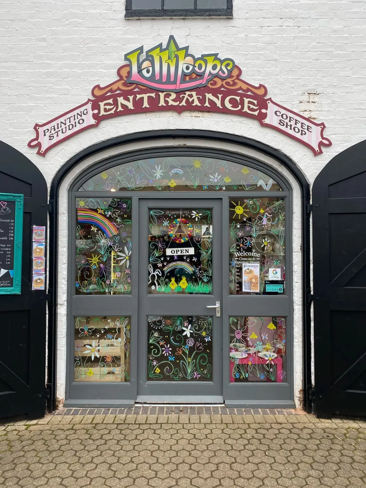 Colourful storefront entrance with decorative painted windows displaying artwork and an ornate red and yellow sign above.