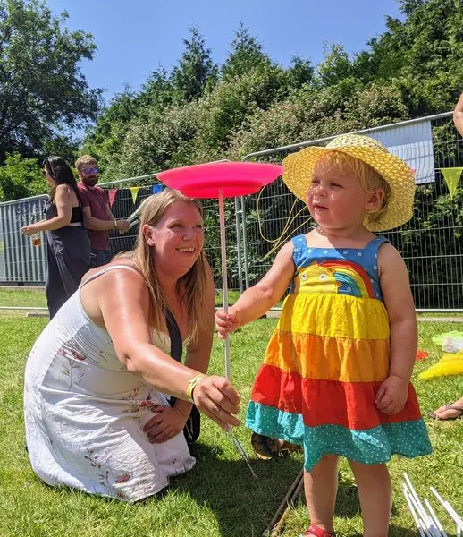 Adult and young child holding a red frisbee during circus skills activity on a sunny grass area.
