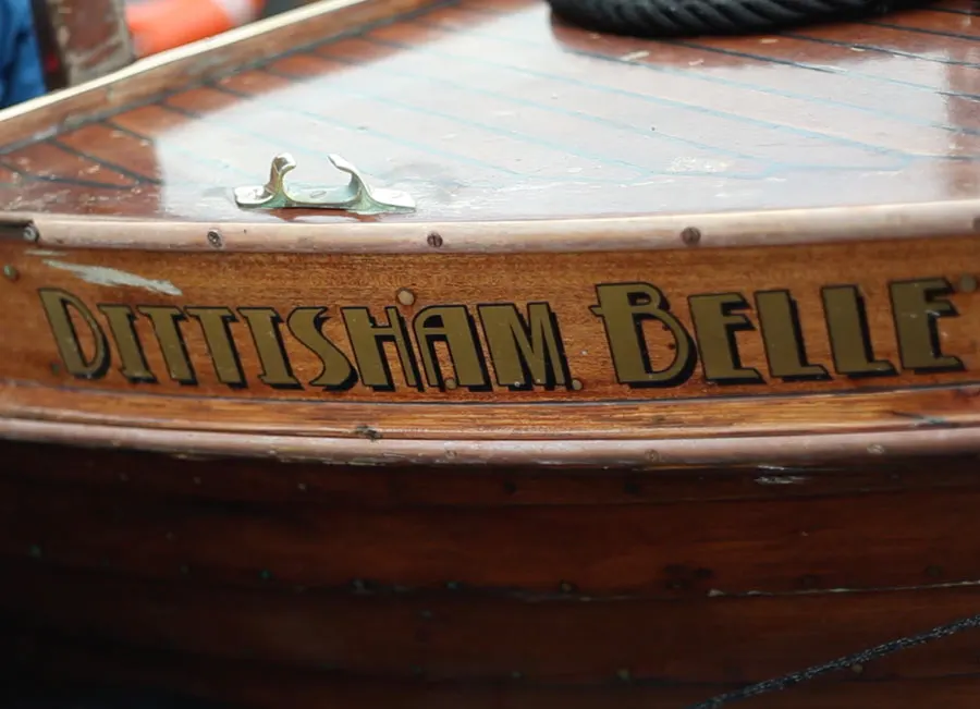 Close-up of wooden boat's hull showing "Dittisham Belle" nameplate with a mooring rope visible.
