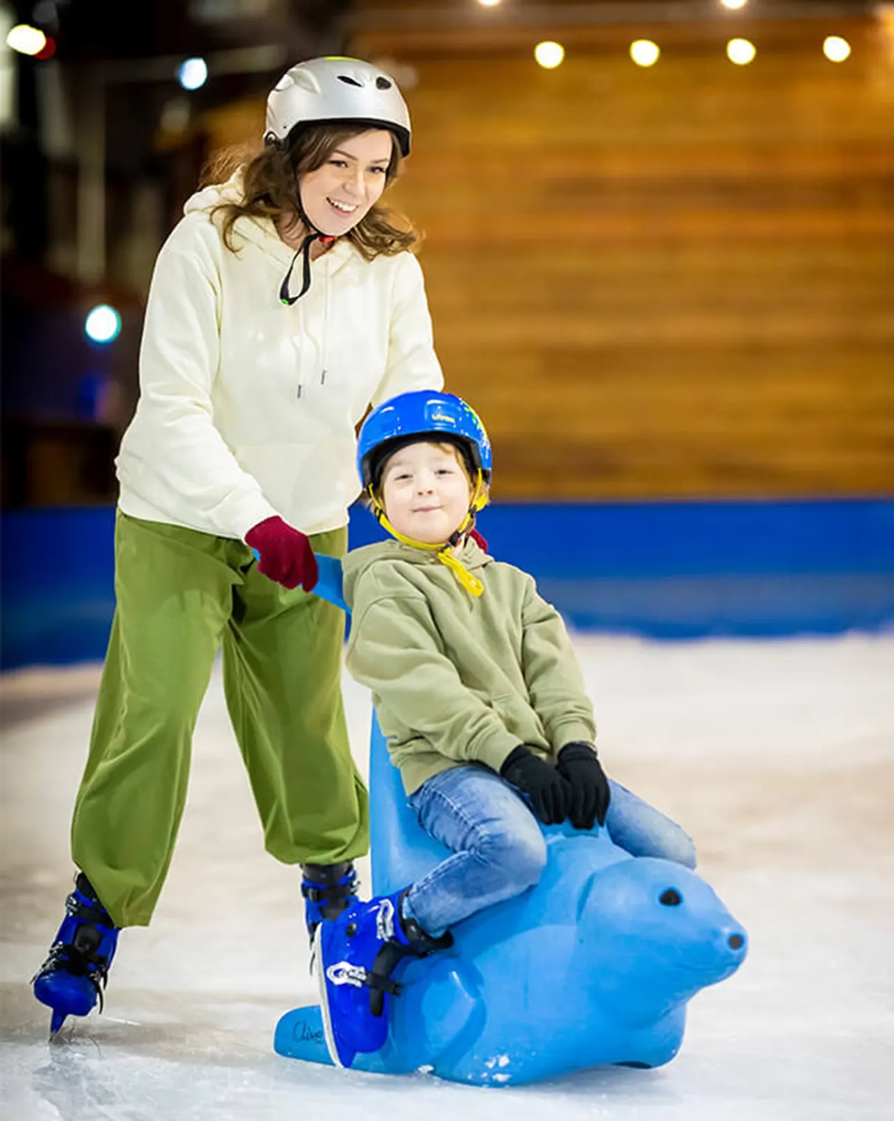 Woman and young child ice skating together, child sitting on a blue skating aid.