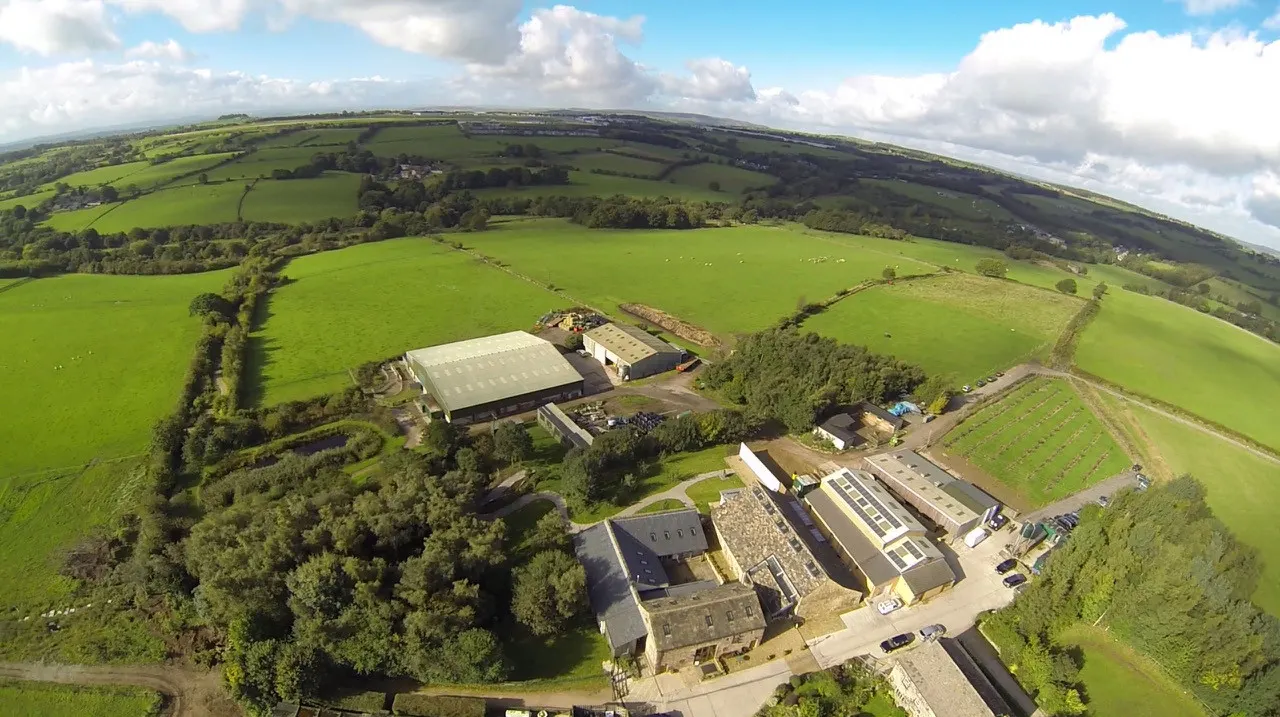 Aerial view of a working farm with stone buildings, modern structures, and surrounding green fields with grazing livestock.
