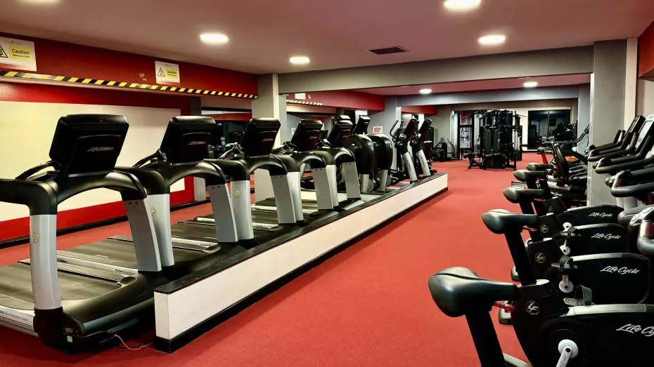 Gym interior with rows of treadmills, exercise bikes and cardio equipment on red flooring.