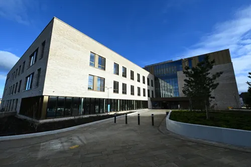 Modern multi-storey library building with white and dark façade beside paved plaza under blue sky.