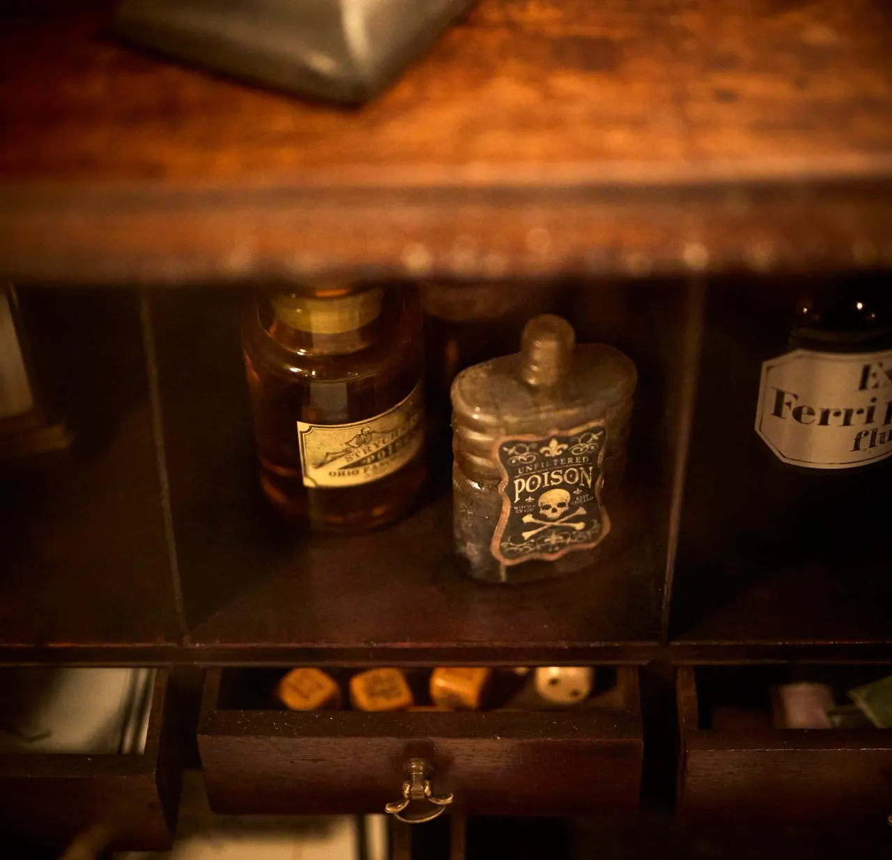 Antique glass bottles with aged labels displayed in a wooden cabinet, including a poison bottle with skull and crossbones marking.