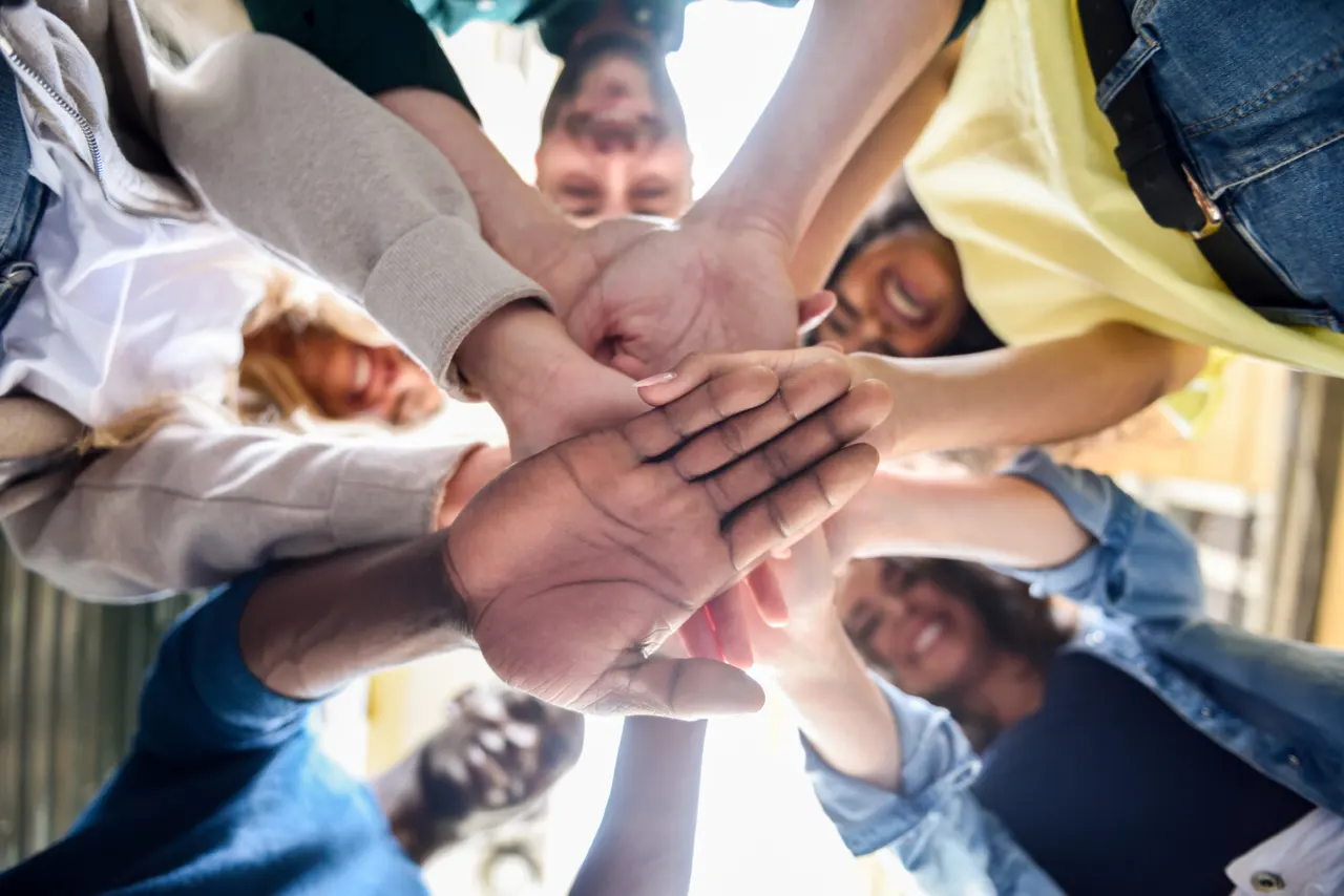 Group of children and adults joining hands together in a circle outdoors.