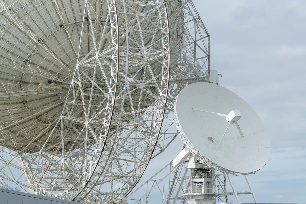 This is a photograph, not a designed graphic.

Large radio telescope dishes with white metal lattice structures and support frameworks against a cloudy sky.