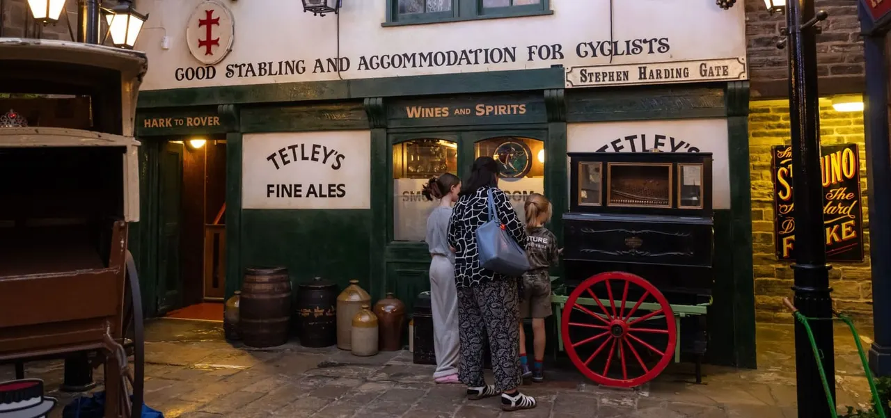 Woman and two children viewing a historic pub storefront display advertising fine ales and accommodation for cyclists.