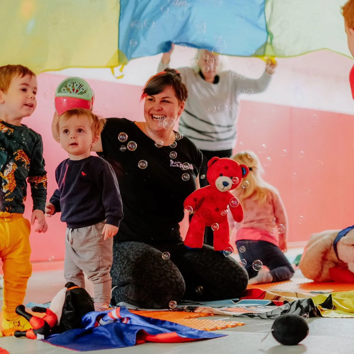 Adult and toddlers playing together in a colourful sensory room with bubbles, toys and parachute.