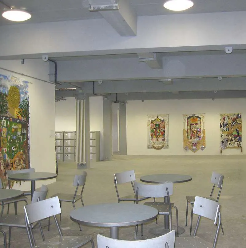 Interior of a community hall with round tables, white chairs, and colourful artwork displayed on cream walls.