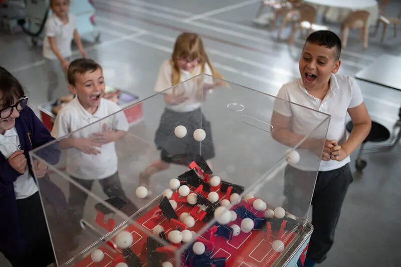 Children playing with an interactive ball-rolling exhibit inside a modern science centre.
