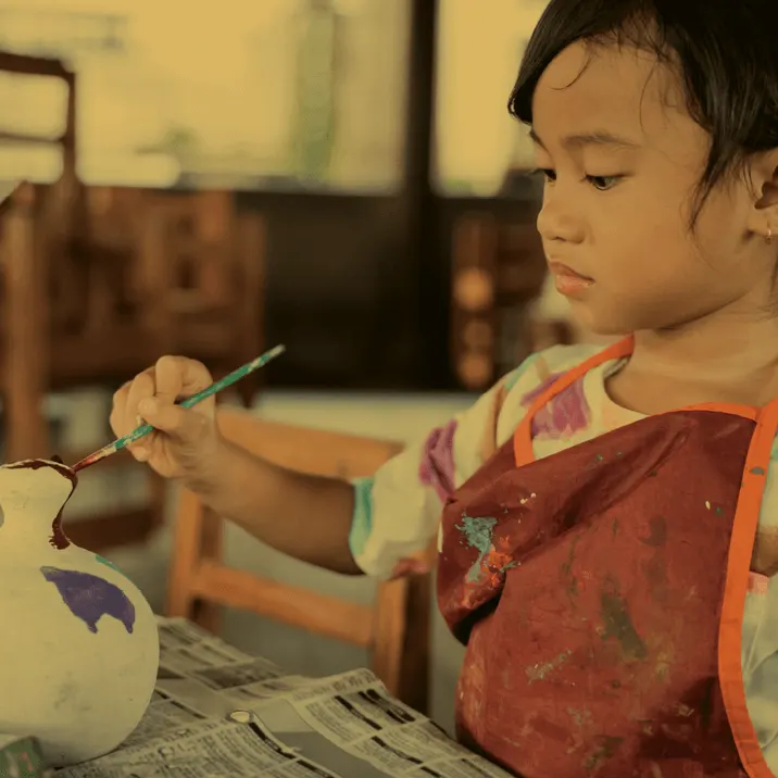 Young child painting a ceramic piece with a brush at a pottery painting studio.