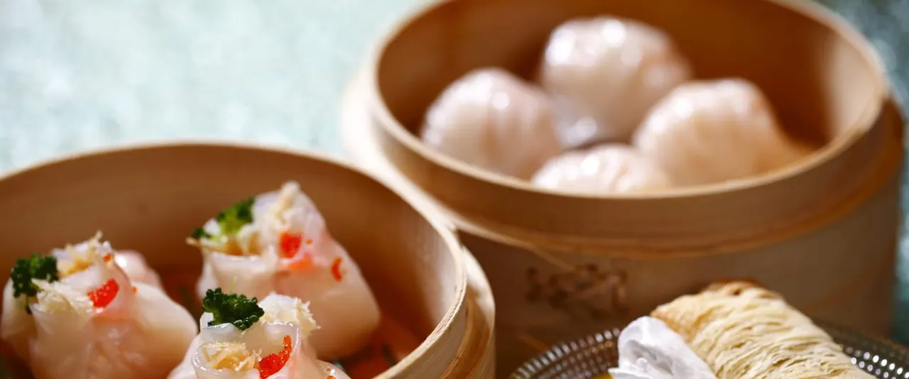 Steamed dumplings with red pepper and coriander garnish in bamboo baskets, served with a side basket of plain dumplings.