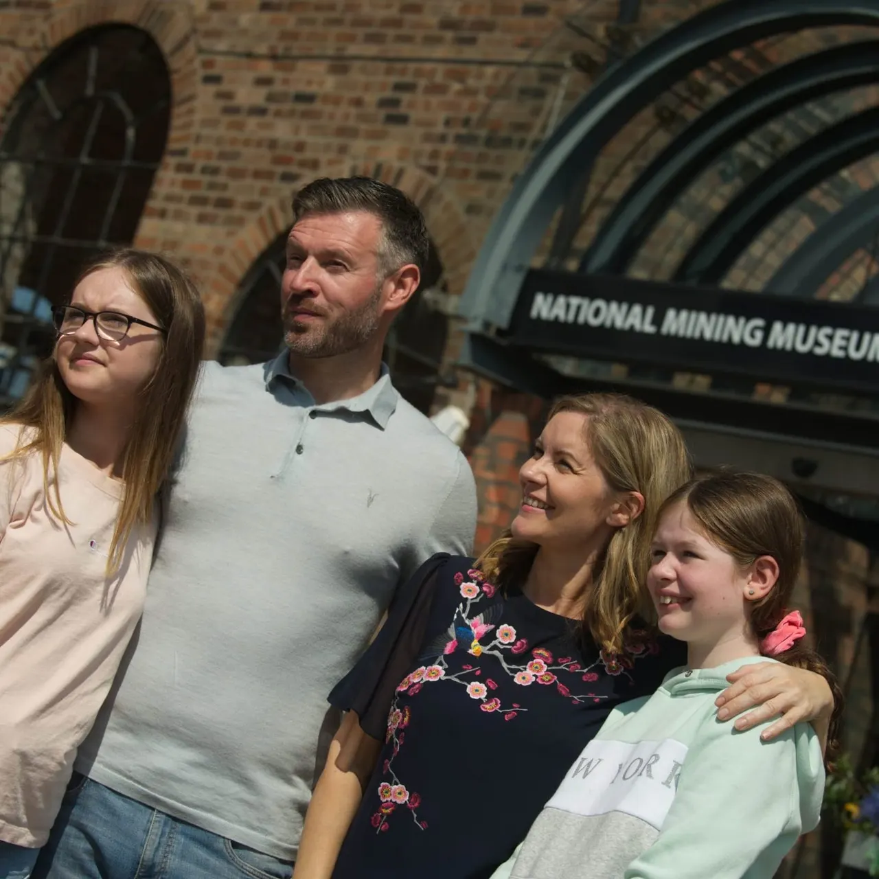 Family of four standing outside brick building entrance to National Mining Museum Scotland.