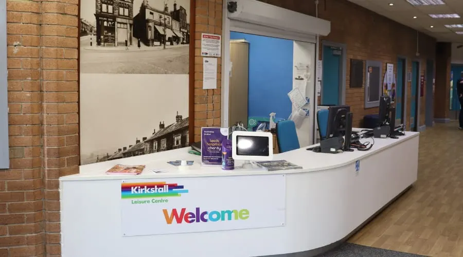 Reception desk with staff counter at Kirkstall Leisure Centre, featuring informational materials and computer equipment.