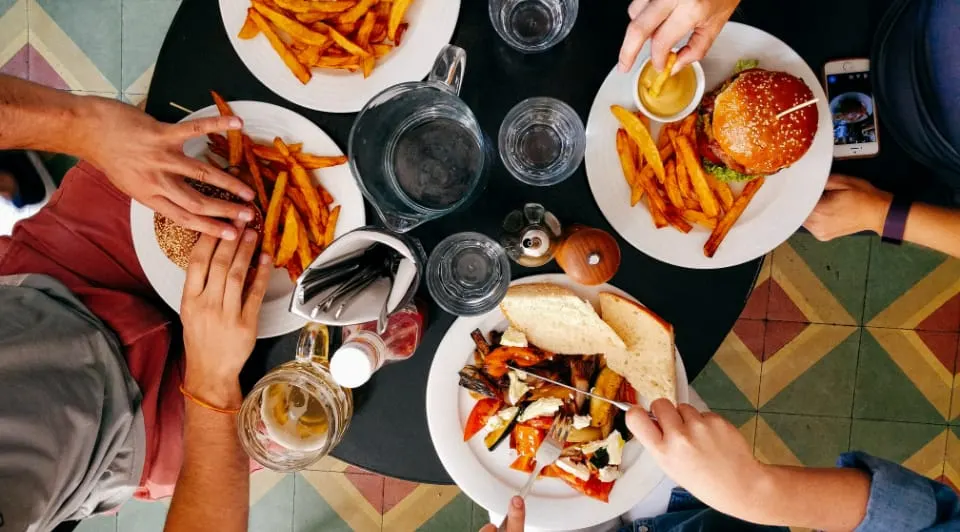 Overhead view of people sharing burgers and chips with glasses of water at a table.