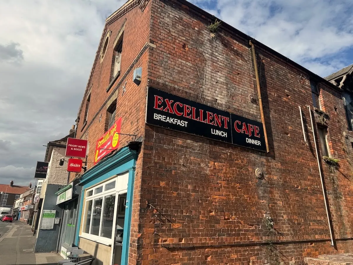 Red brick cafe building with turquoise door and signage advertising breakfast, lunch and dinner services.