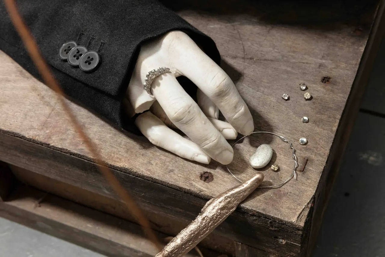 Hands with a diamond ring displaying jewellery and metalwork pieces arranged on wooden surface.