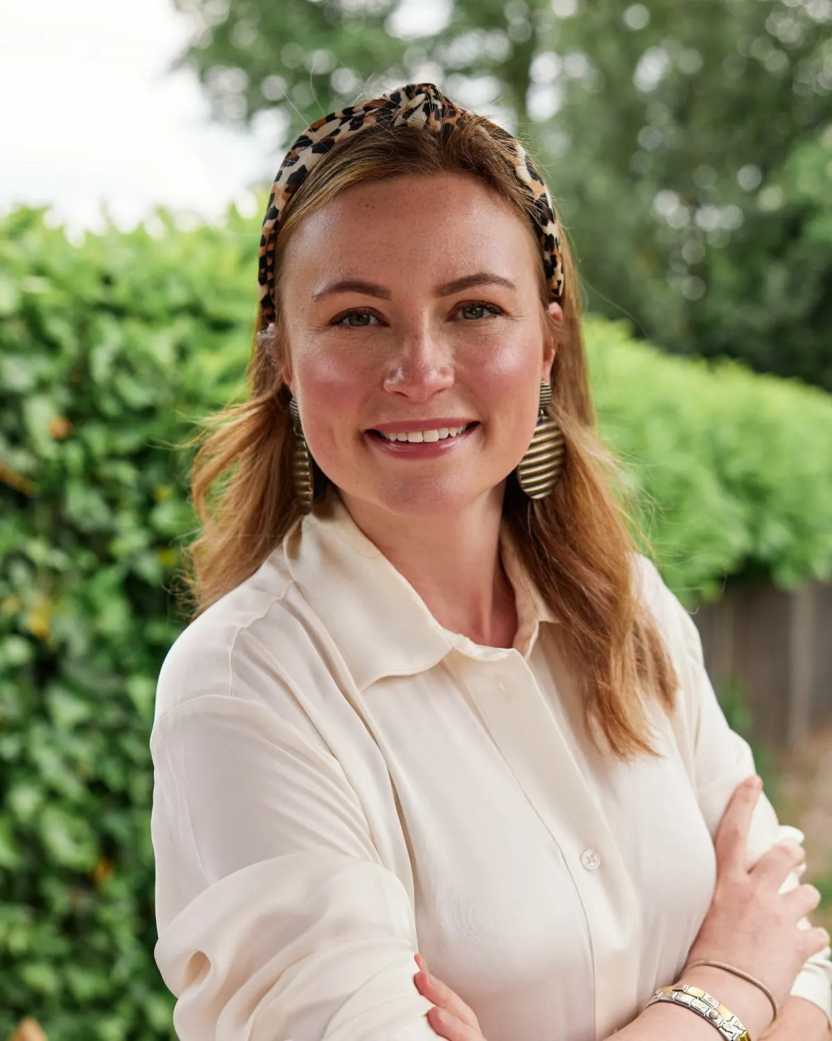 Woman smiling at camera in a garden setting with green foliage behind her.