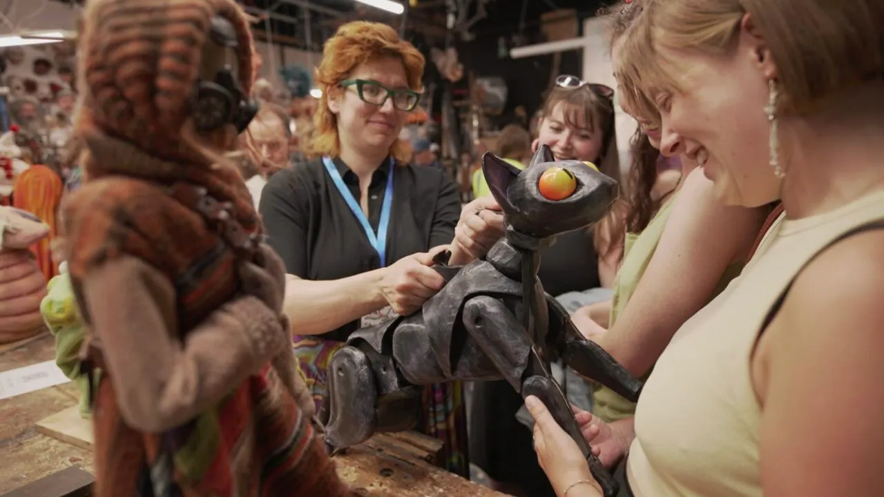 Visitors examine and handle elaborate puppet figures at an indoor event or workshop venue.