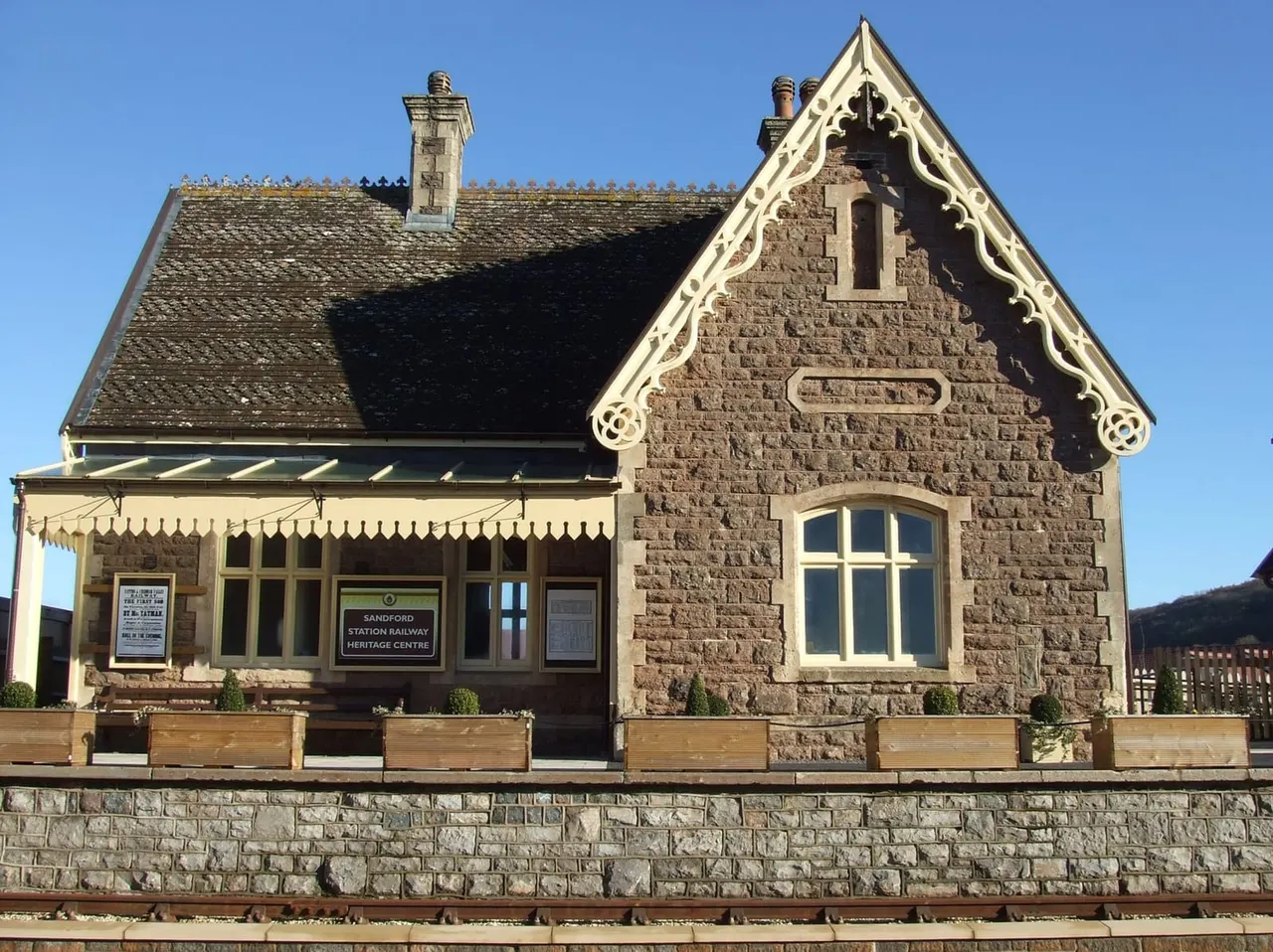 Victorian stone railway station building with cream trim and pitched roof against clear blue sky.