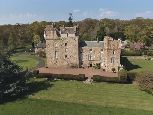 Medieval stone castle with turrets surrounded by manicured grounds, trees and flowering shrubs in spring.