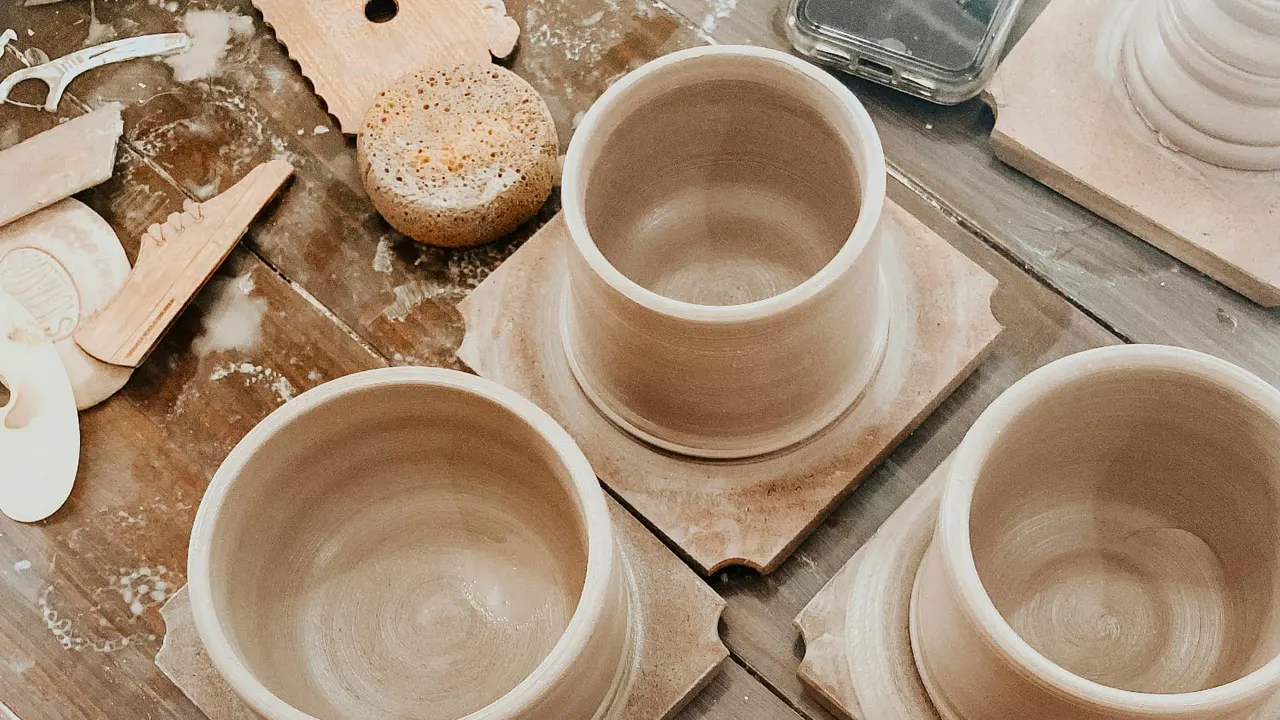 Pottery workshop tabletop with empty clay bowls and vessels in progress, wooden tools, and flour-dusted work surface.