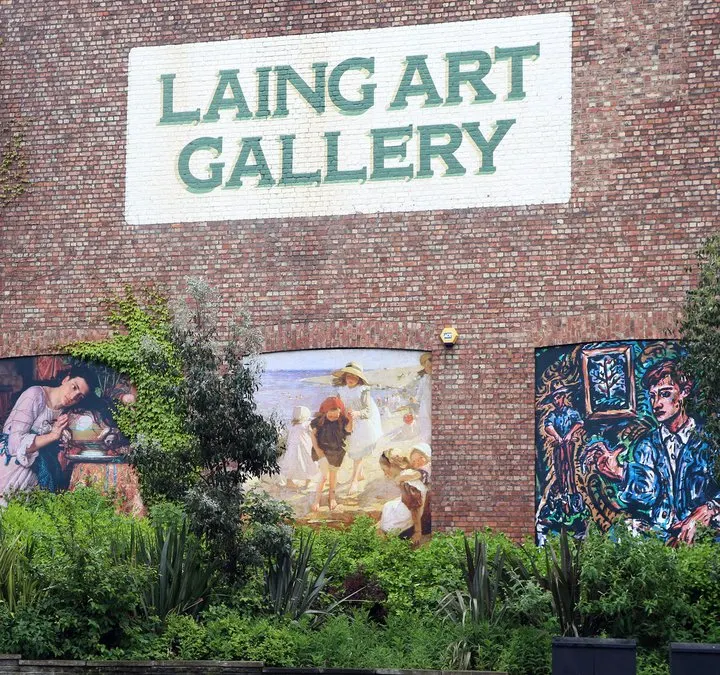 Red brick building exterior with "Laing Art Gallery" signage and painted artworks displayed on the wall above planted greenery.