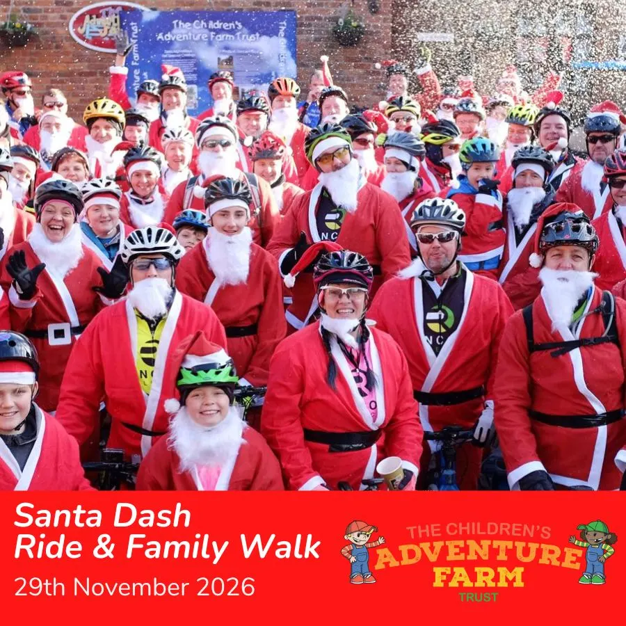 Large group of cyclists dressed as Father Christmas wearing red suits, white beards and cycle helmets, posing together outdoors against a brick wall with confetti falling.