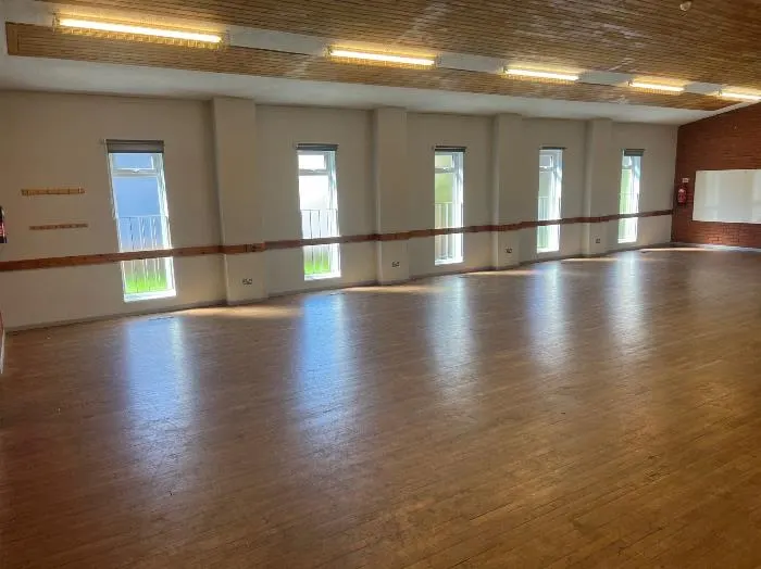 Empty dance or exercise studio with wooden floor, mirrored wall and tall windows.