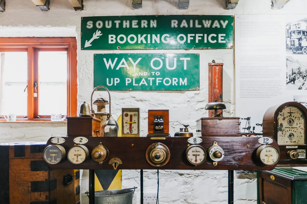 Vintage railway signage and control panels displayed on a white-walled museum interior, with an orange-framed window and historical photographs.