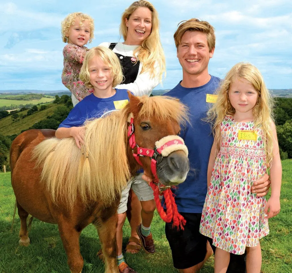 Family with two adults and three children posing with a pony in a rural hillside setting.