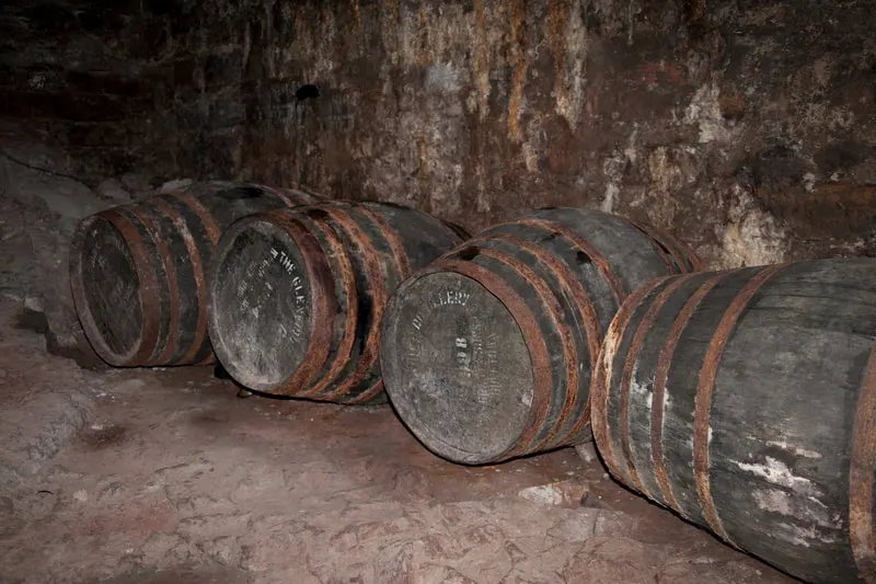 Wooden barrels with metal bands lying on the ground against a weathered stone wall in a cellar or dungeon.