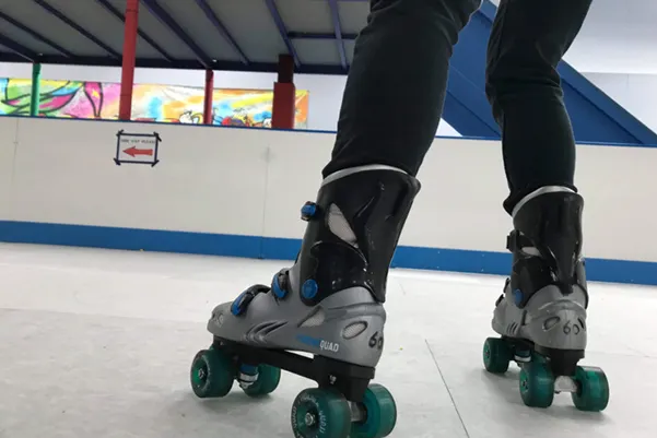 Person wearing roller skates with green wheels on an indoor skating rink.