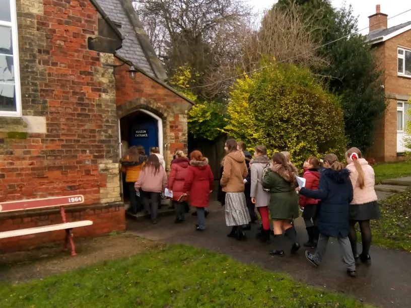 Visitors queuing outside a red brick museum building with a blue entrance door during autumn.