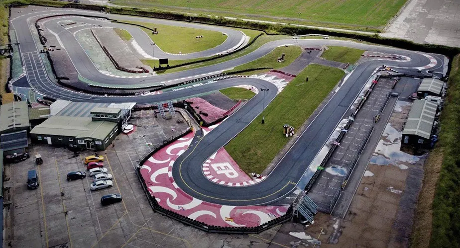 Aerial view of a go-kart racing circuit with track, buildings, and parked cars.