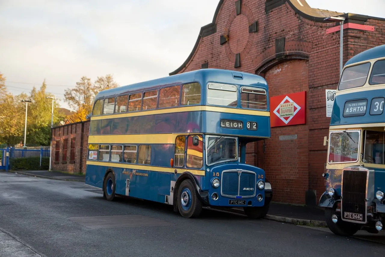 Restored vintage double-decker buses displayed outside a brick transport museum building in autumn.