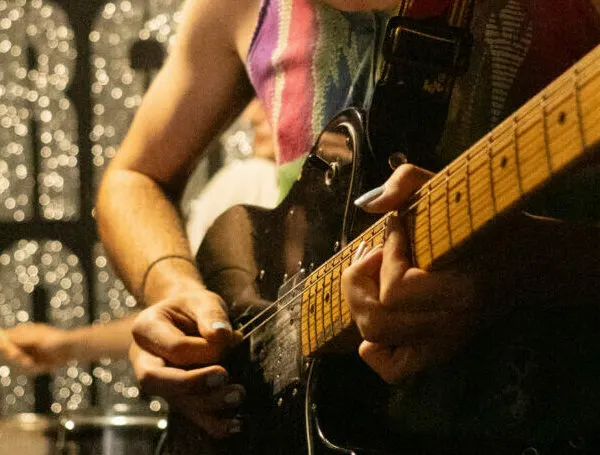 Musician playing electric guitar on stage with shimmering backdrop lights behind.
