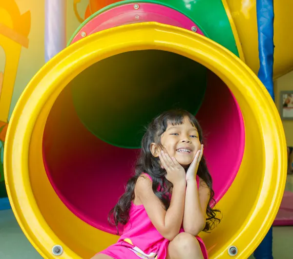 Young child smiling inside a colourful play tunnel at an indoor play area.
