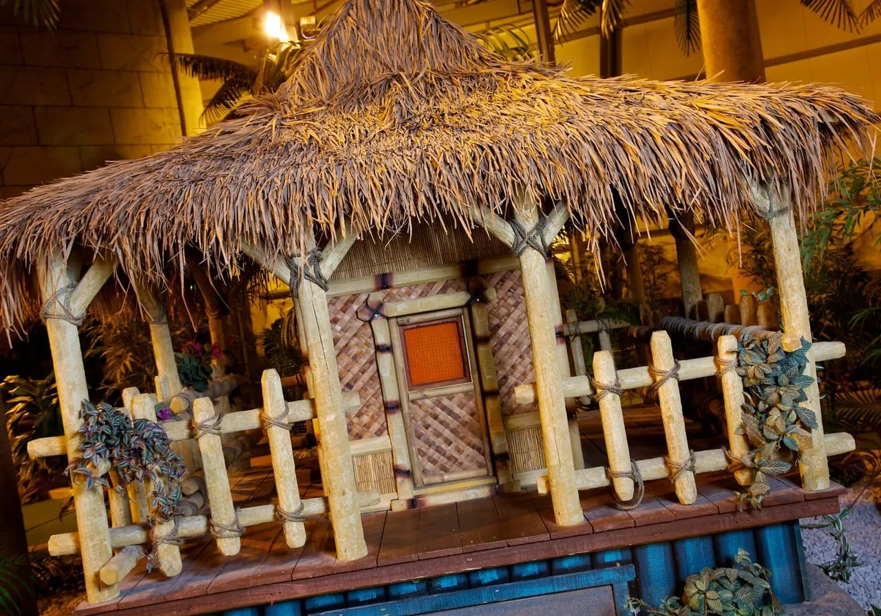 Thatched-roof tropical hut display with wooden fence and decorative plants at indoor adventure golf venue.